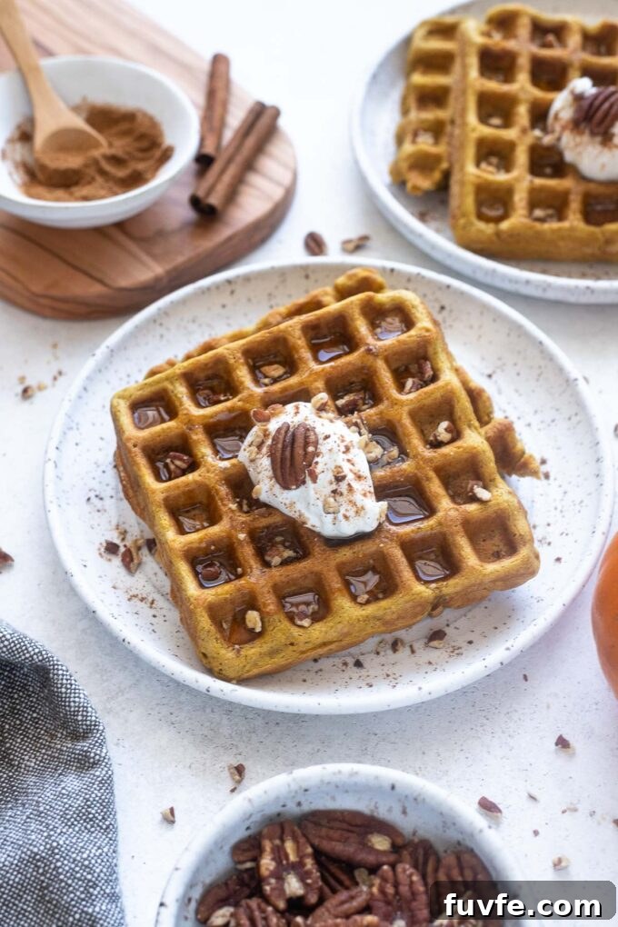 Pumpkin spice waffles on a plate with dollop of yogurt and pecans.