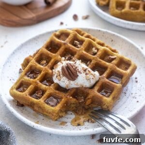 Pumpkin spice waffles on a plate with pecans and maple syrup.