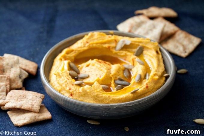 A dish of kabocha squash hummus surrounded by pita chips, on a dark blue background.