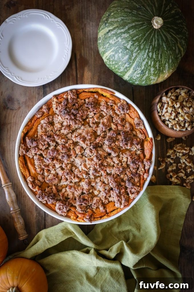 Overhead view of a kabocha squash casserole. A whole squash and a dish of nuts rest nearby.