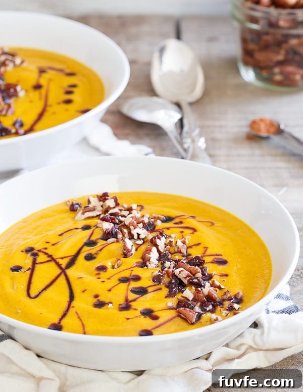 Two bowls of kabocha squash soup topped with pecans and a cherry drizzle.