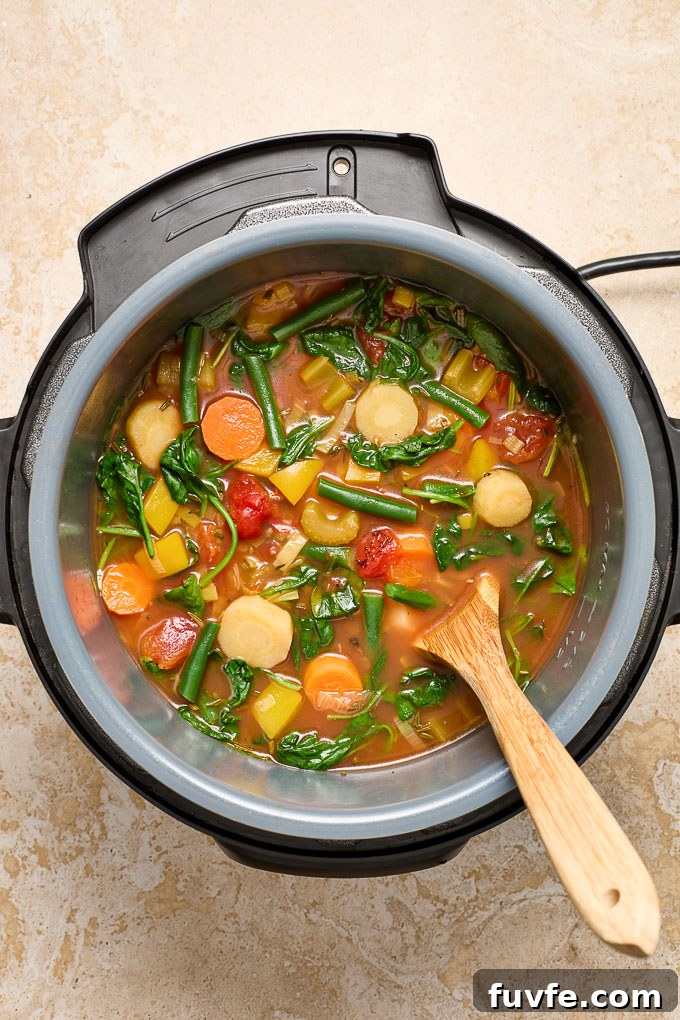Vegetable soup in Instant Pot with a wooden spoon