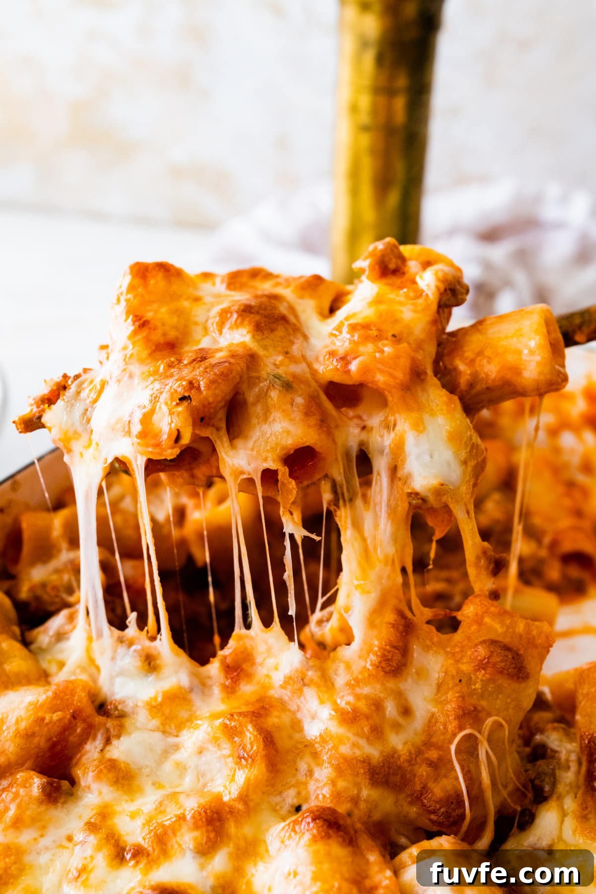 baked cheesy classic pasta al forno recipe out of the oven in a white baking pan. Serving spoon lifting up the pasta al forno with a cheese pull.