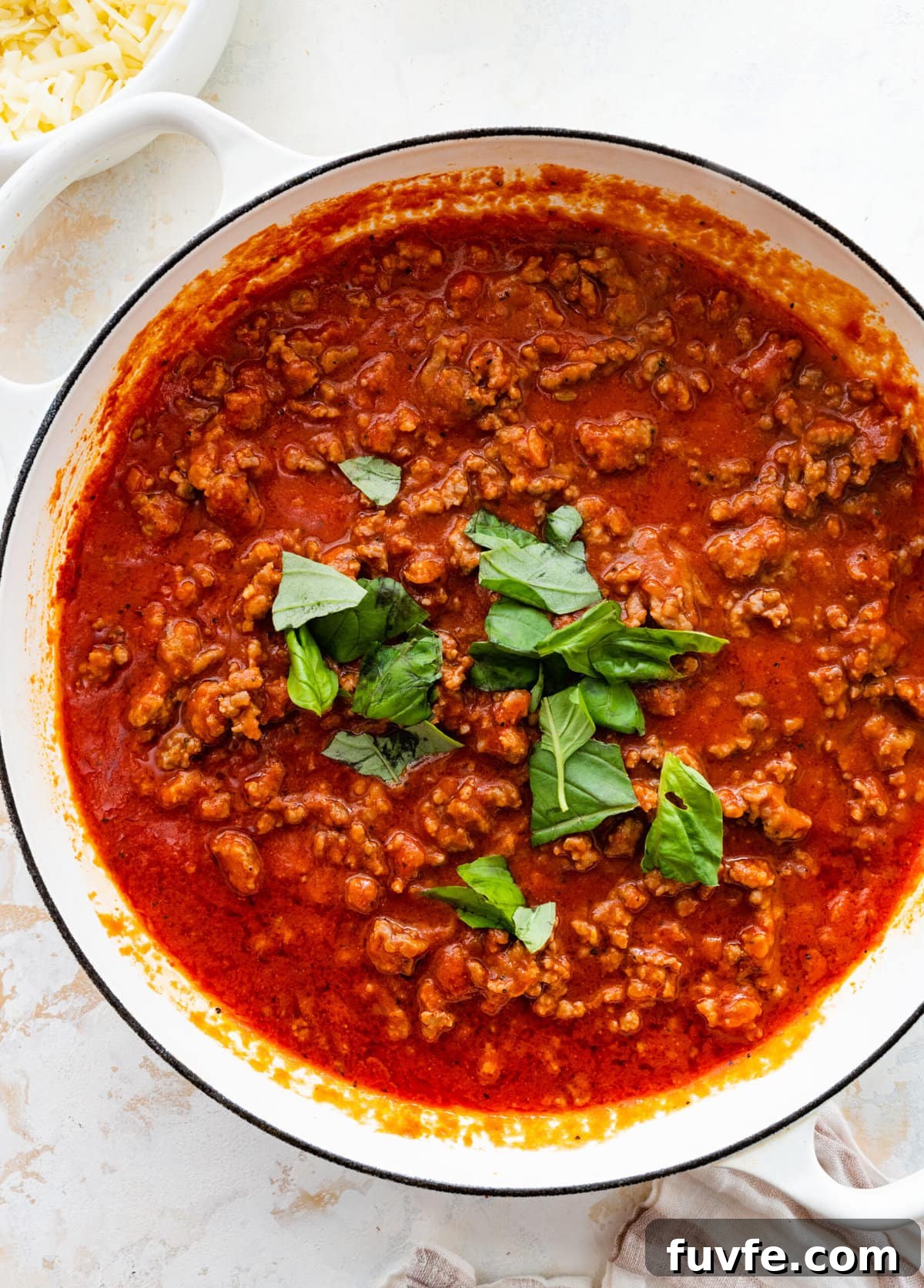 How to make classic pasta al forno step-by-step: adding basil to the pan with meat and sauce.