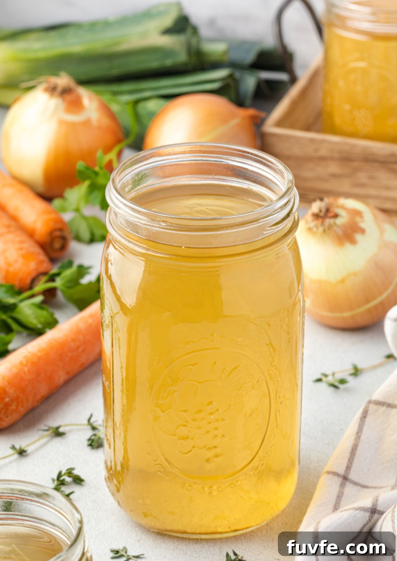Homemade vegetable broth in a jar surrounded by veggies