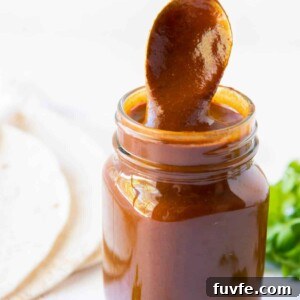 A glass jar of homemade enchilada sauce with a spoon stirring the sauce.