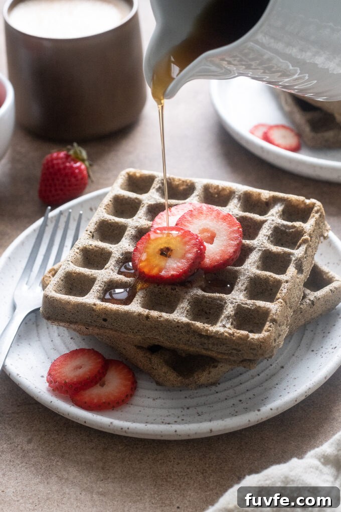 Buckwheat waffles on a plate with maple syrup pouring over them.
