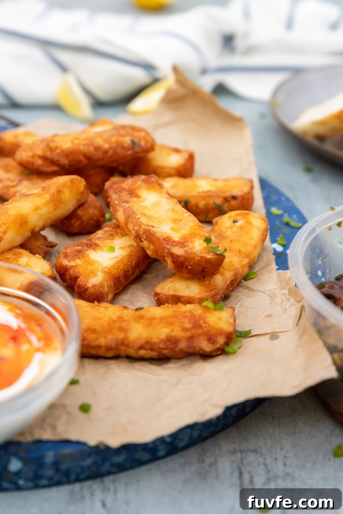 Crispy Halloumi Fries Recipe: Golden, Crunchy Cheese Fries 2 A stack of halloumi fries on brown paper and a blue marble platter with dips to the side