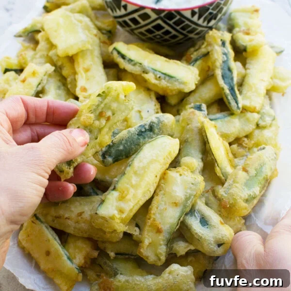 Crispy Halloumi Fries Recipe: Golden, Crunchy Cheese Fries 8 A hand dipping a zucchini fry from a big plate of them into tzatziki sauce