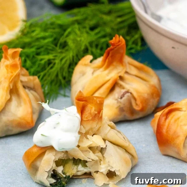 Crispy Halloumi Fries Recipe: Golden, Crunchy Cheese Fries 10 Crispy spinach and feta filo parcels, one with a bite out of it to show the spinach and feta filling inside, all on baking paper with ingredients behind.