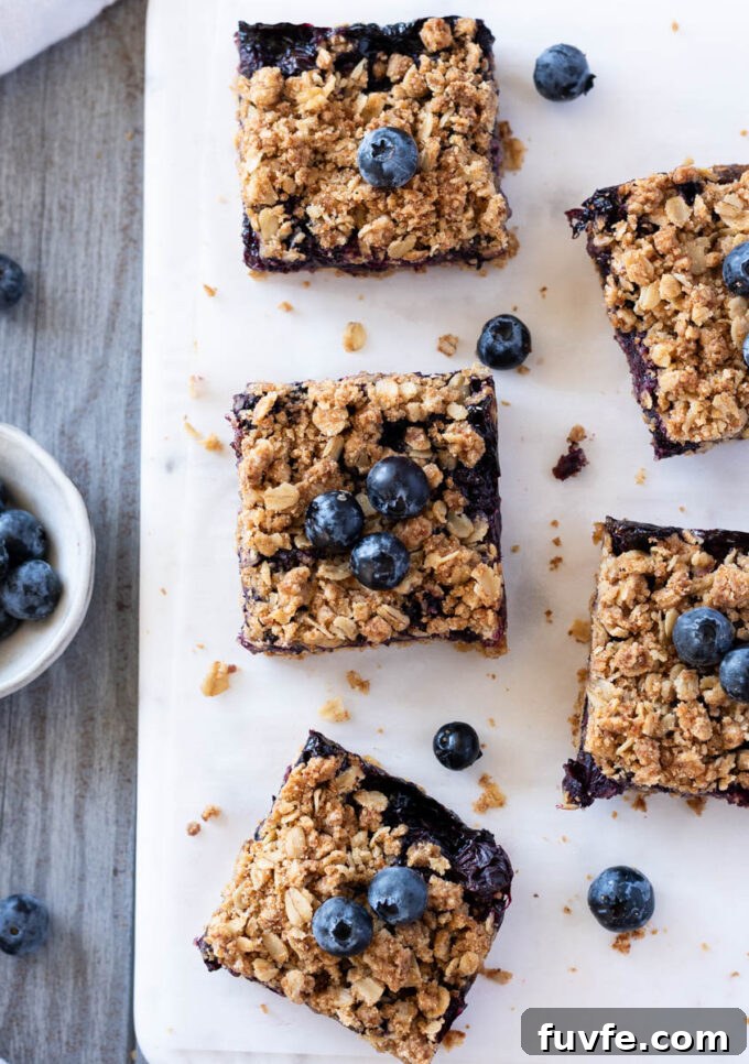 Blueberry Crumble Bars Recipe with Oat Crust 3 Blueberry crisp bars on a board with fresh blueberries.