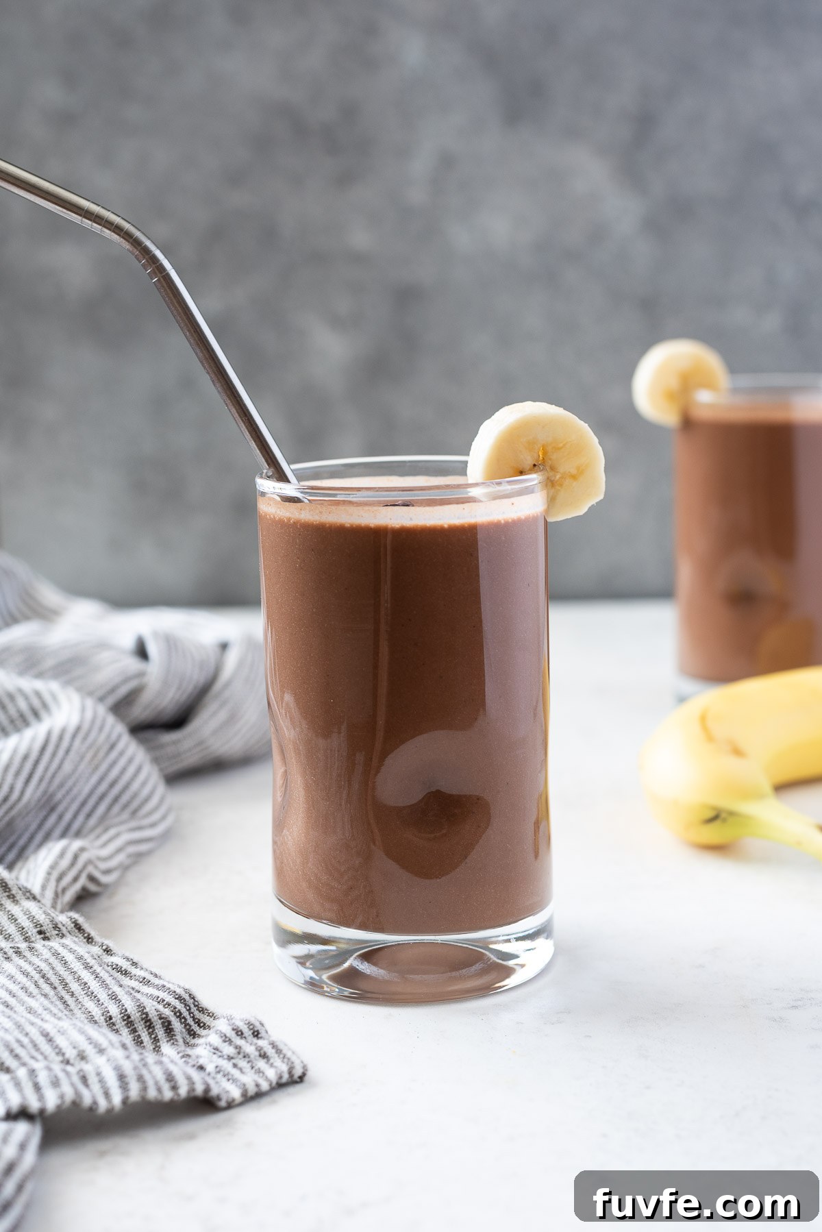 chocolate protein smoothie in a glass with banana slice on the rim