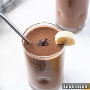 close up of chocolate banana protein smoothie with metal straw and banana on rim