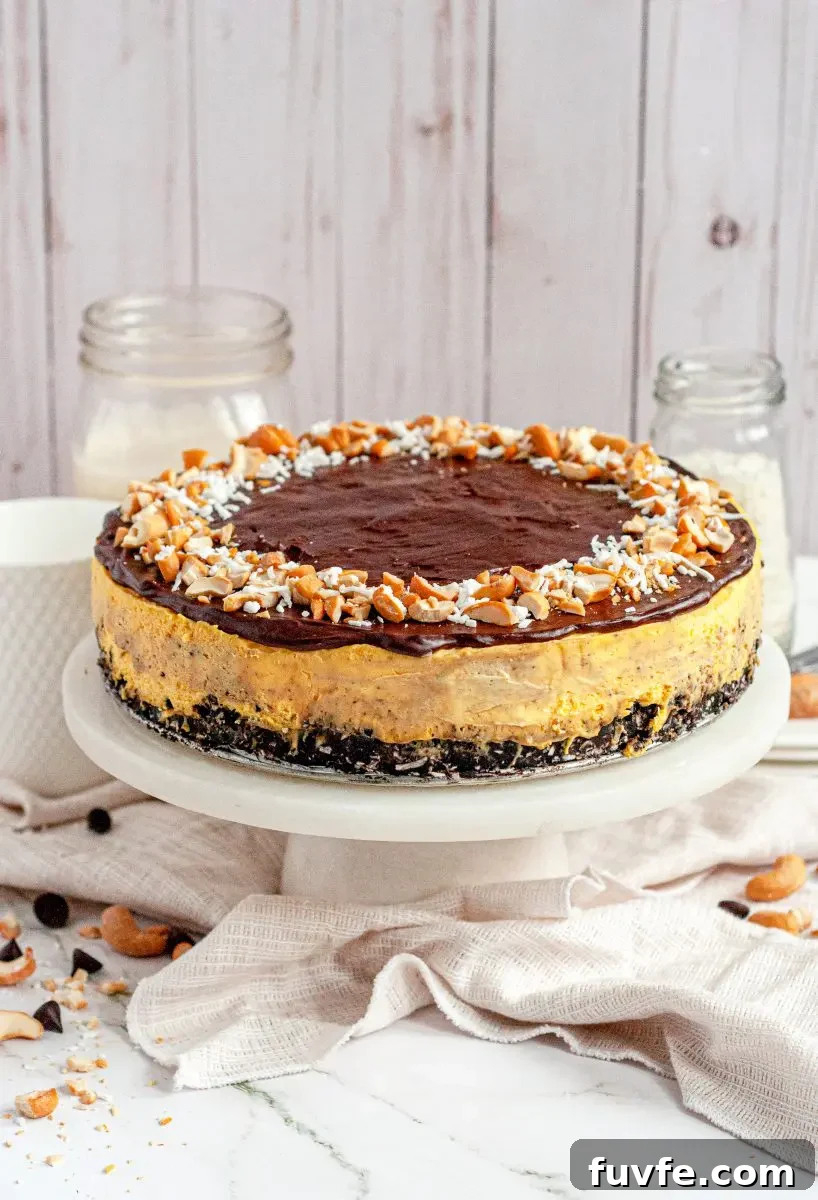 A no-bake nanaimo bar cheesecake. it has three layers. The bottom layer is a chocolate crust, the middle layer is a yellow custard cheesecake, and the top is a thin layer of dark chocolate topped with white shredded coconut and yellow salted cashews.