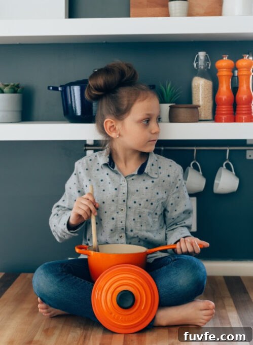A small child sitting on a table with a pot and wooden spoon.