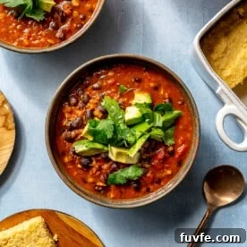 A single serving of chili sits in a brown bowl on a blue countertop.