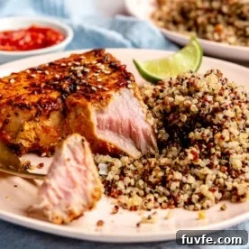 A gold fork with a bite of ahi tuna laying on a light pink plate