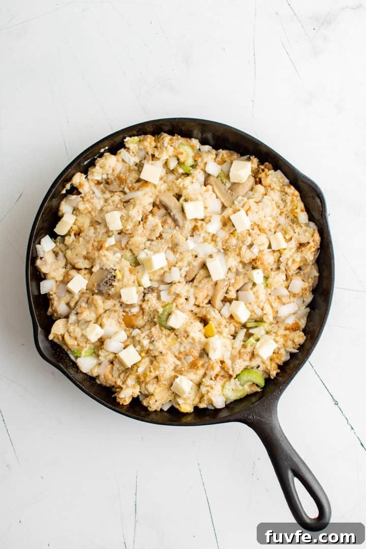 Savory Sage Stuffing Recipe for Thanksgiving and Roast Dinners 7 Unbaked stuffing in cast iron dotted with butter.