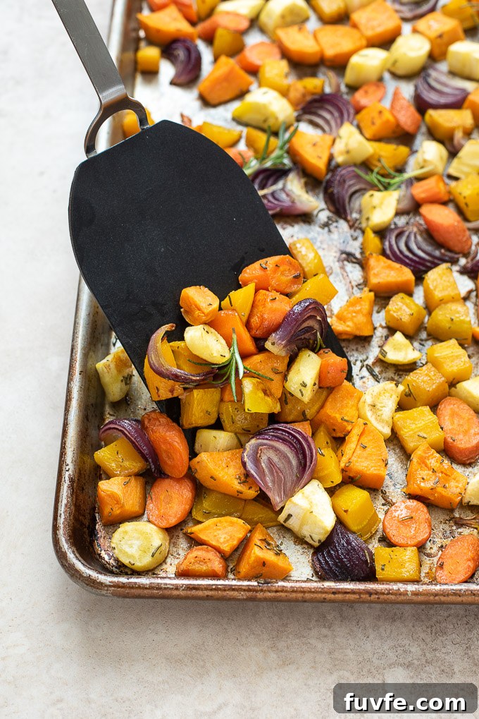 Spatula scraping off roasted root vegetables on a sheet pan