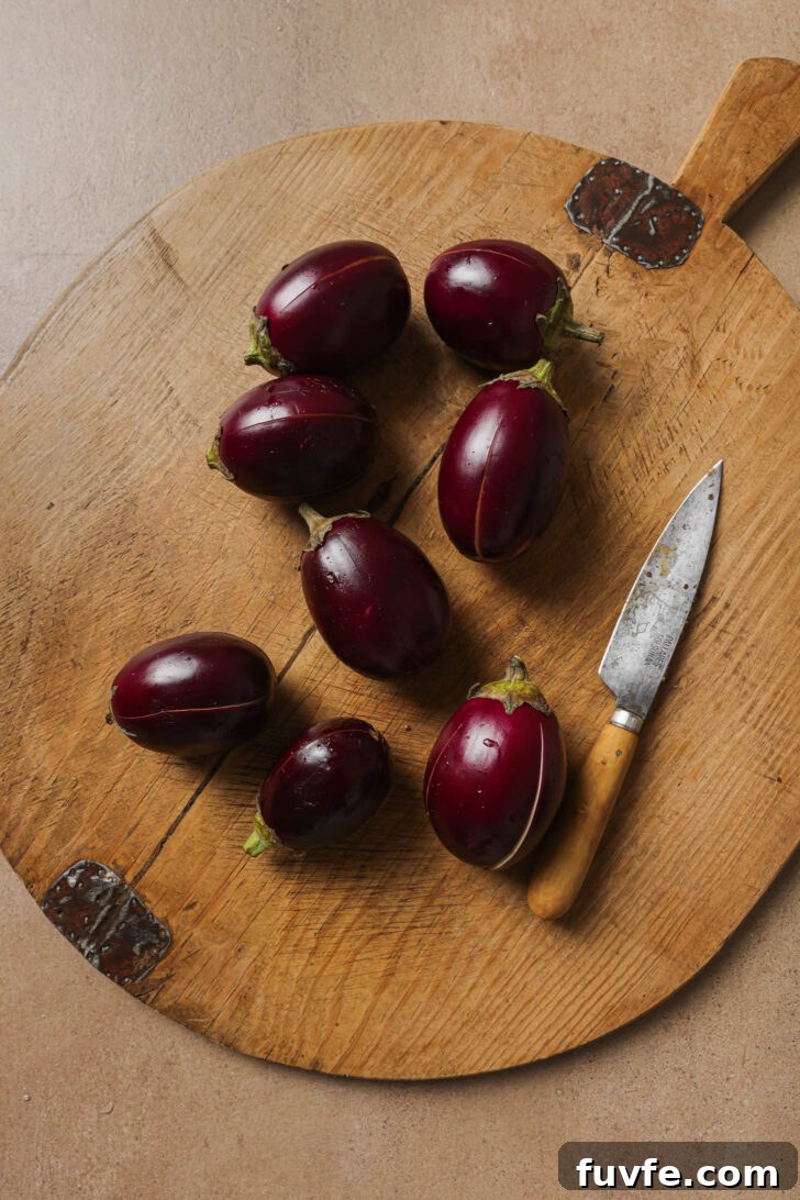 Slit baby eggplants on a wooden cutting board with a knife.