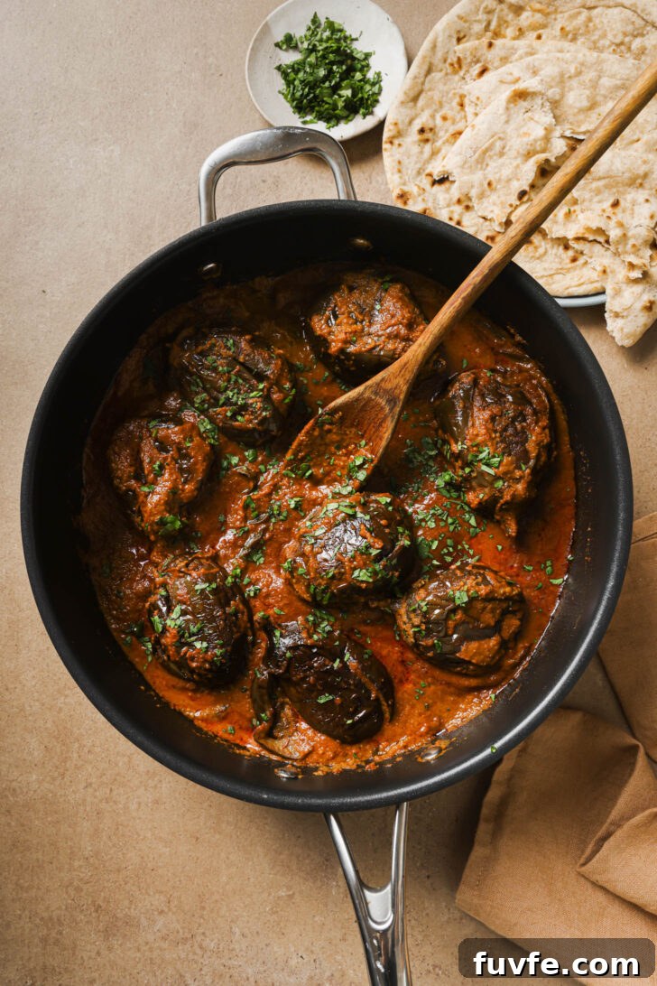 Bagare Baingan in a skillet with a wooden spoon garnished with minced cilantro.