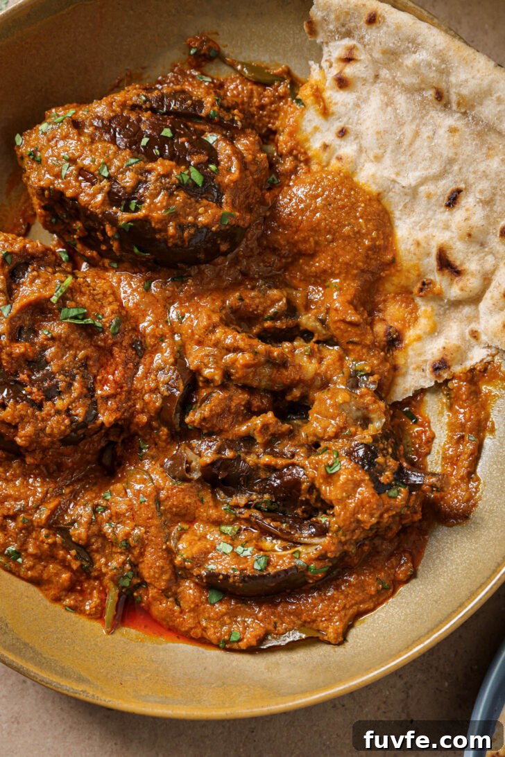 Close up of Bagare Baingan in a plate with a piece of roti garnished with minced cilantro.