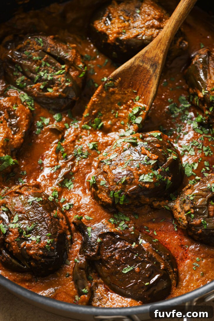 Close up of Bagare Baingan in a skillet with a wooden spoon garnished with minced cilantro.