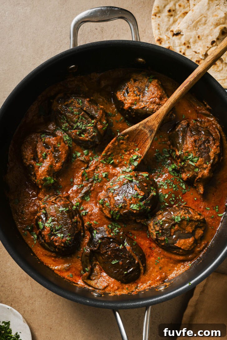 Bagare Baingan in a skillet with a wooden spoon garnished with minced cilantro.
