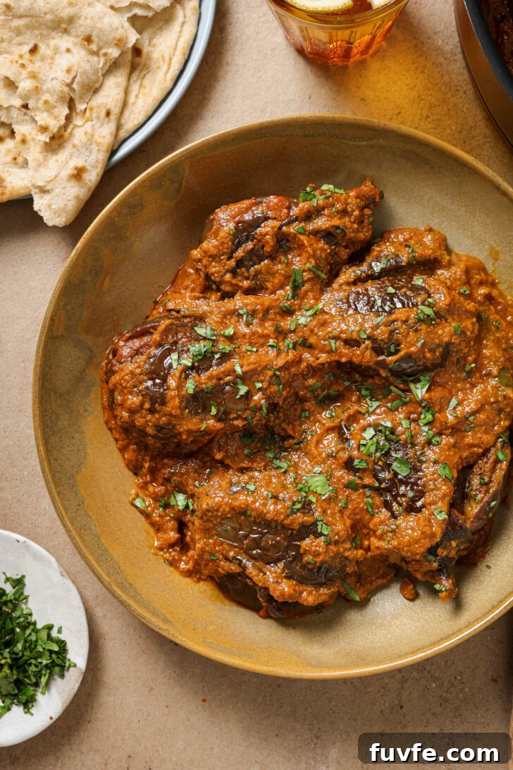Bagare Baingan in a plate garnished with minced cilantro with a plate of roti on the side.