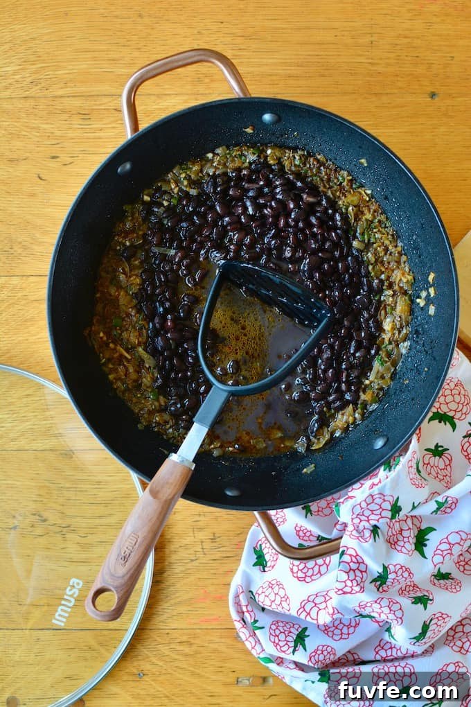Quick Canned Black Beans Recipe for Flavorful Weeknight Meals 2 A black pot filled with black beans and a potato masher inside the pot.
