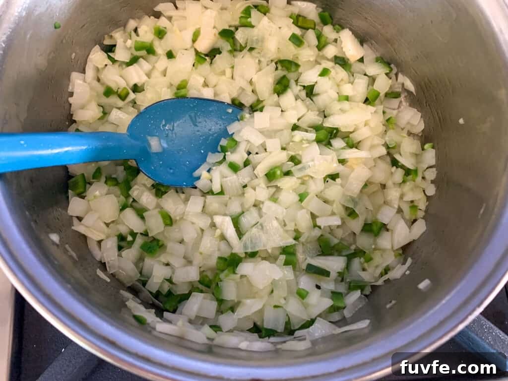 Quick Canned Black Beans Recipe for Flavorful Weeknight Meals 5 A metal saucepan with onions, jalapeños, and garlic sauteing in it and a blue spoon stirring the mixture.