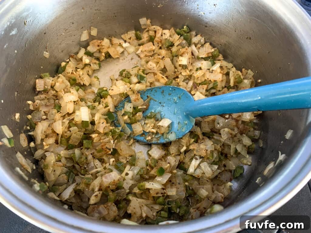 Quick Canned Black Beans Recipe for Flavorful Weeknight Meals 6 A metal pan with onions, garlic, jalapeno, and spices in it being stirred by a blue spoon.