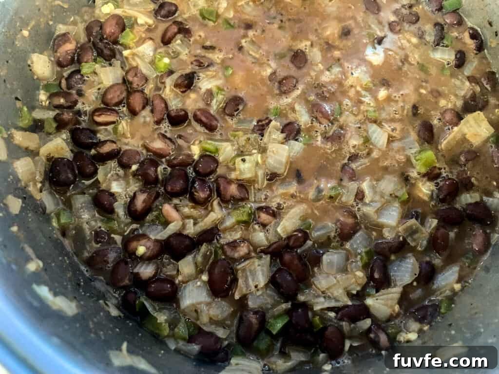 Quick Canned Black Beans Recipe for Flavorful Weeknight Meals 7 A pan of black beans with onions, and jalapeños and garlic in it simmering.
