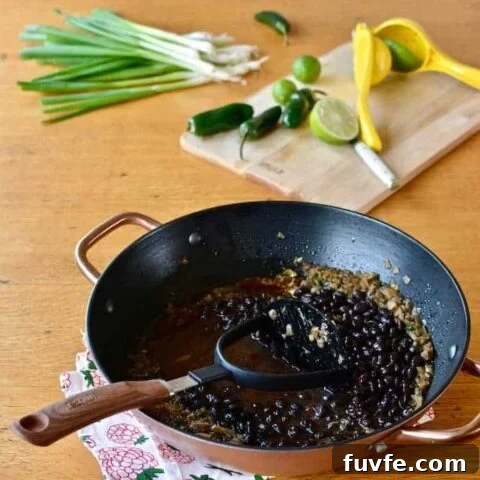 A copper pot of black beans sitting on a table next to a cutting board with limes.