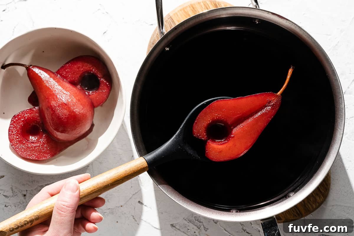 Poached pear being removed from wine with slotted spoon
