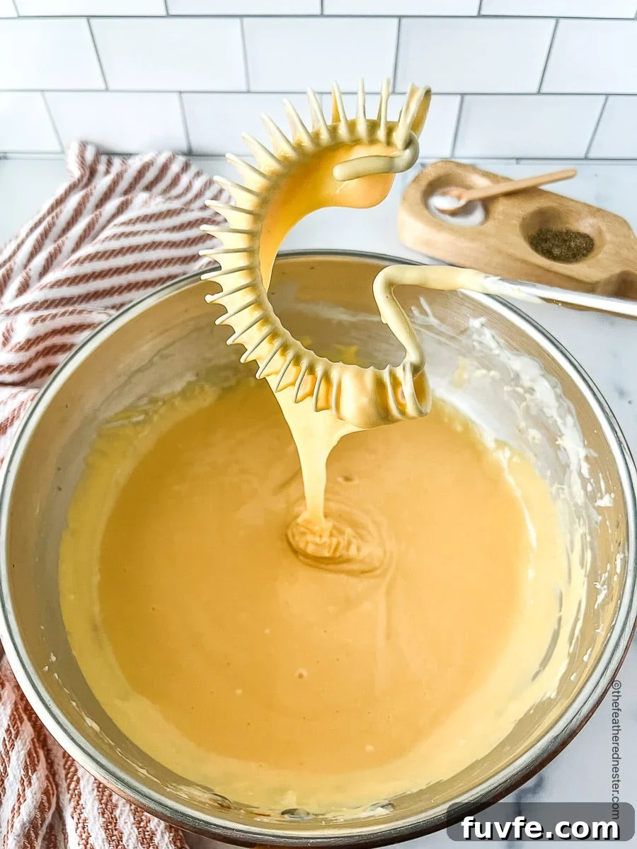 Creamy melted cheddar cheese in a bowl and on a whisk.