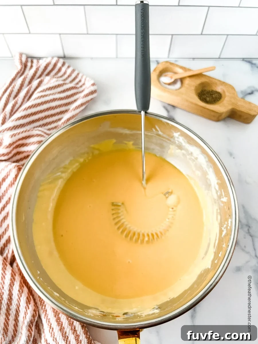 Creamy yellow sauce in a large bowl with a whisk.