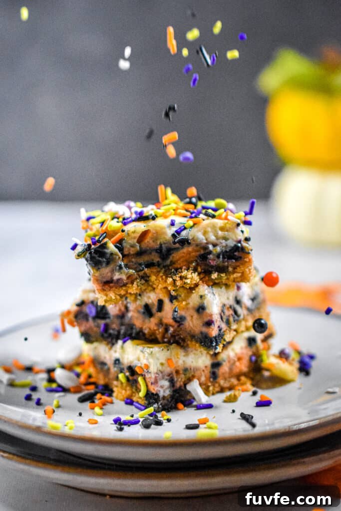 A stack of Halloween cheesecake bars are being sprinkled with sprinkles