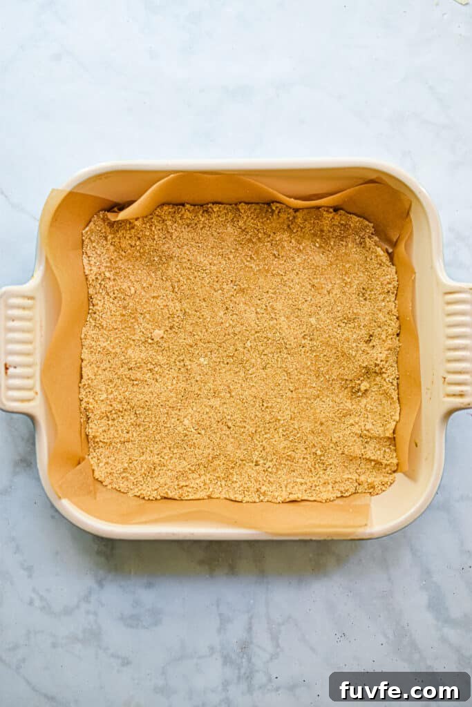 The graham cracker crumbs are added to a 8x8 parchment lined baking dish
