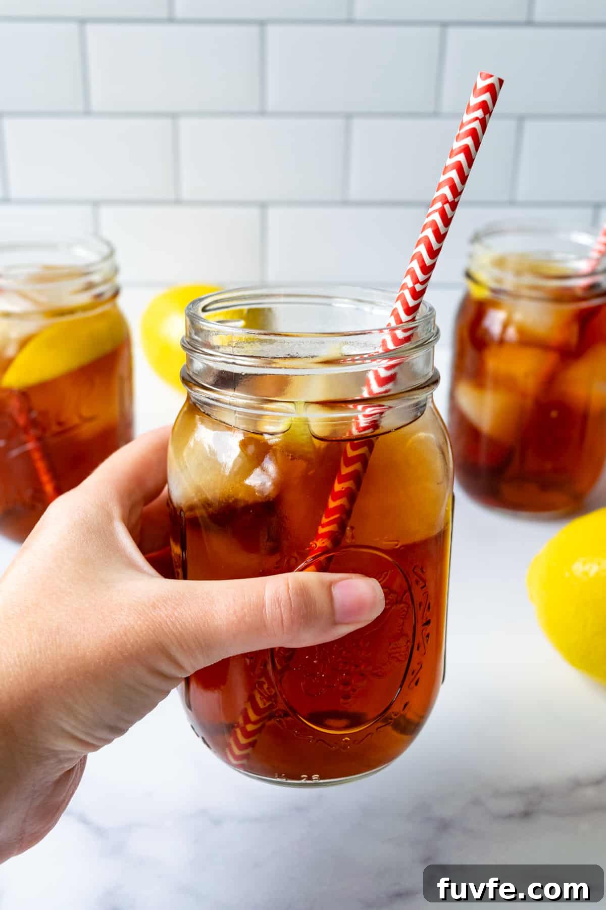A hand holding a mason jar of Earl Grey Iced Tea with a red and white straw.