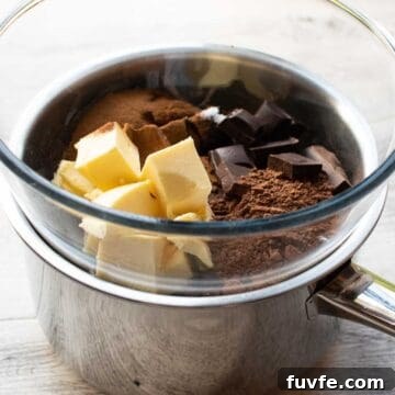 Butter, cocoa powder and chocolate in glass bowl in a steel saucepan.