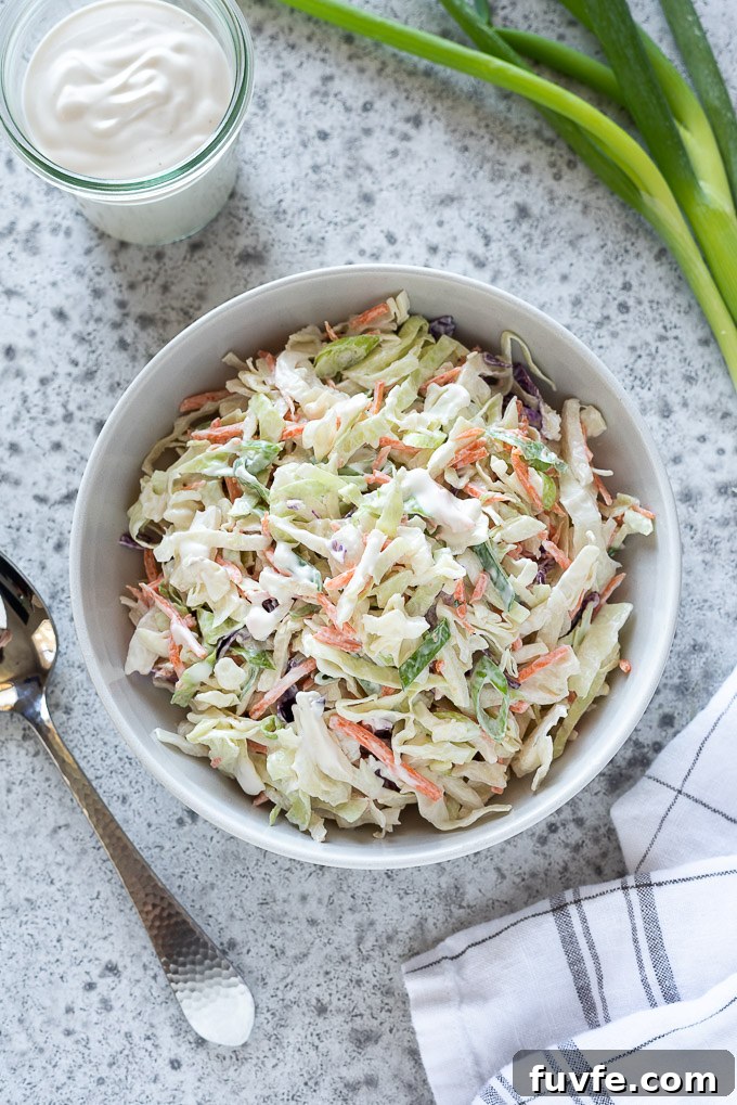 Coleslaw in a white bowl with dressing and green onions