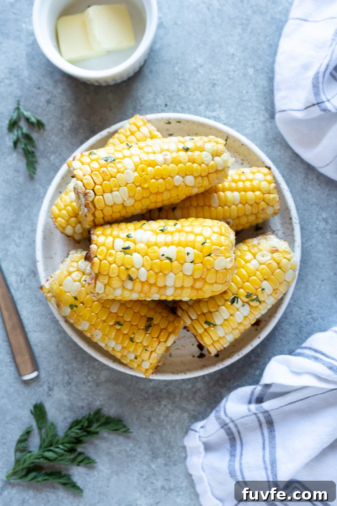 Air fryer corn on the cob on a white plate with butter and parsley