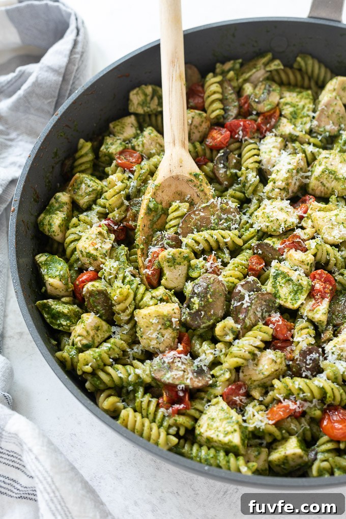 Wooden spoon scooping chicken pesto pasta in skillet