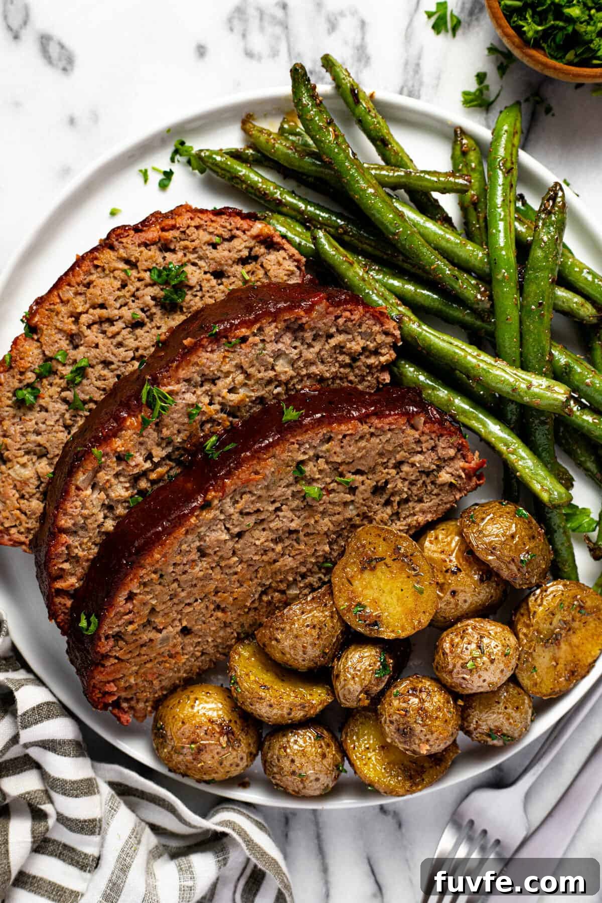 White plate with sliced meatloaf roasted potatoes and green beans.
