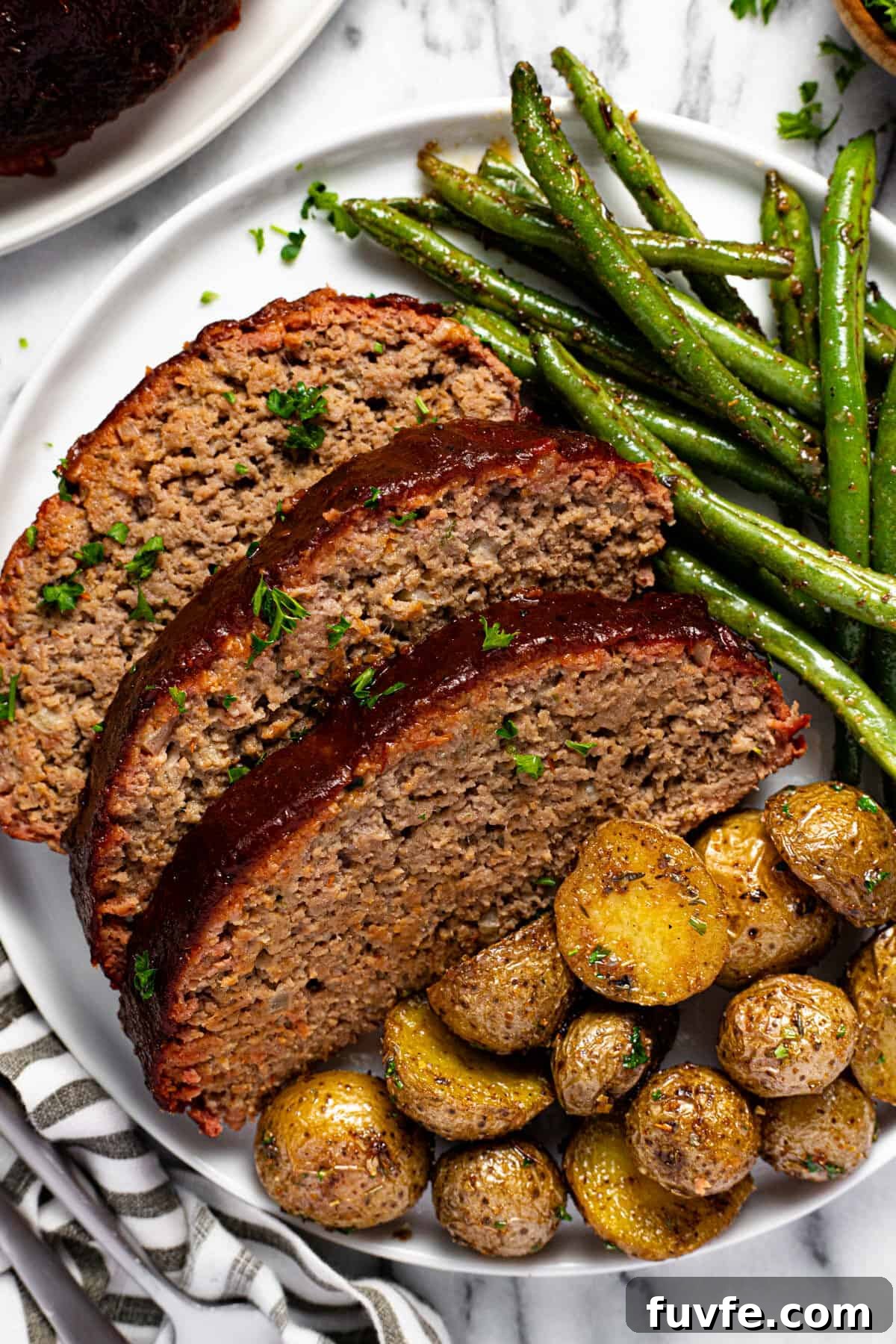 White plate with sliced meatloaf roasted potatoes and green beans.