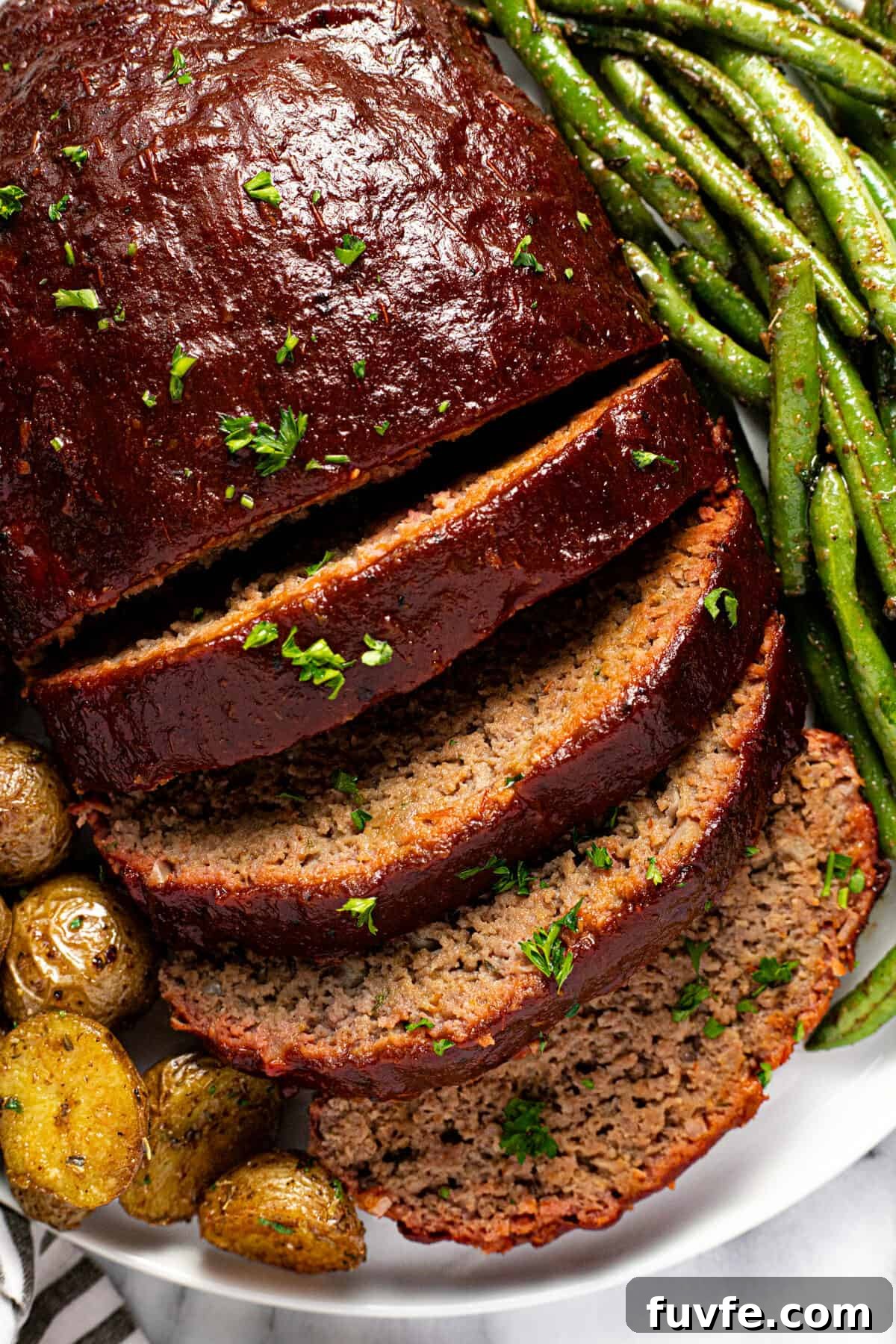 Close up shot of sliced smoked meatloaf on a plate with potatoes and green beans.