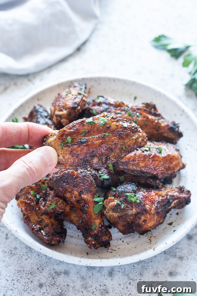 Hand holding air fryer chicken wing above plate of wings