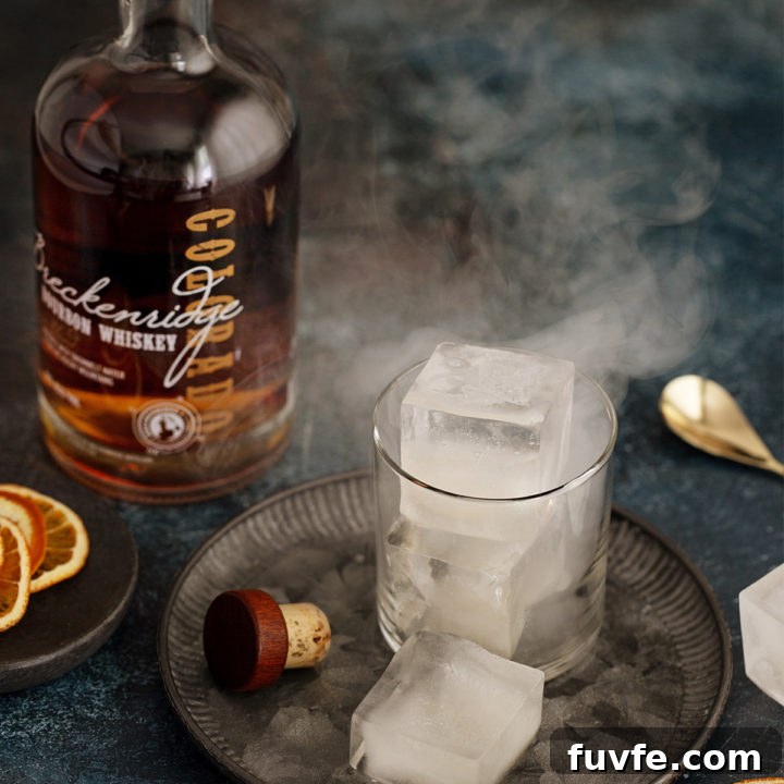 glass of smoked ice cubes next to a bottle of bourbon