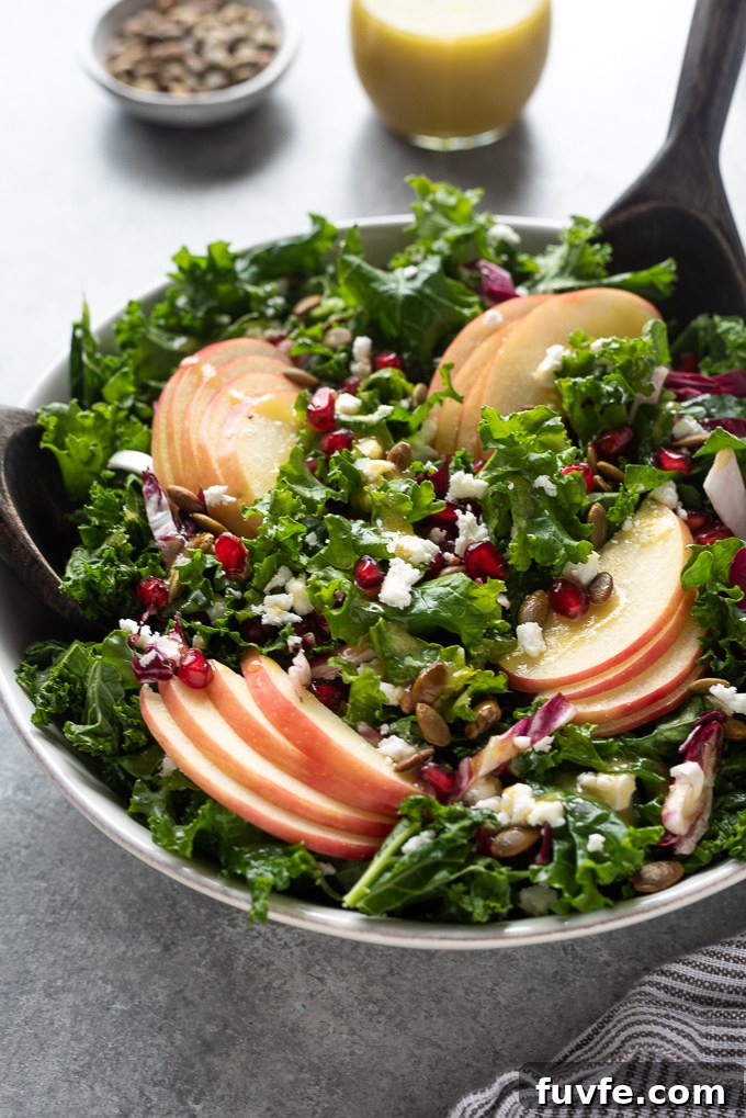 Kale apple salad with salad servers digging into bowl